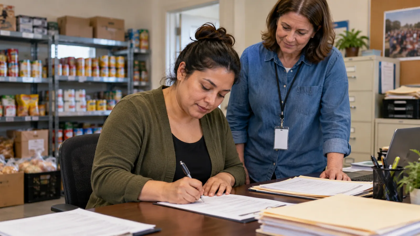 At dusk in a modest U.S. pantry storeroom, a Latina office assistant double-checks an inventory clipboard beside stacked cardboard food boxes, soft overhead light.